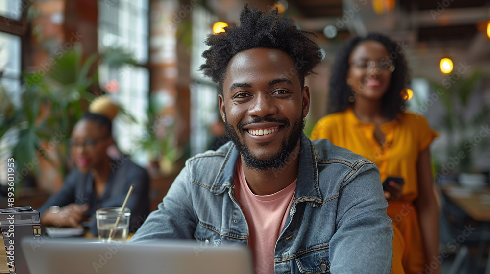 Young black man smiling while working on a laptop in a vibrant plant-filled workspace Young black man smiling while working on a laptop in a vibrant plant-filled workspace
