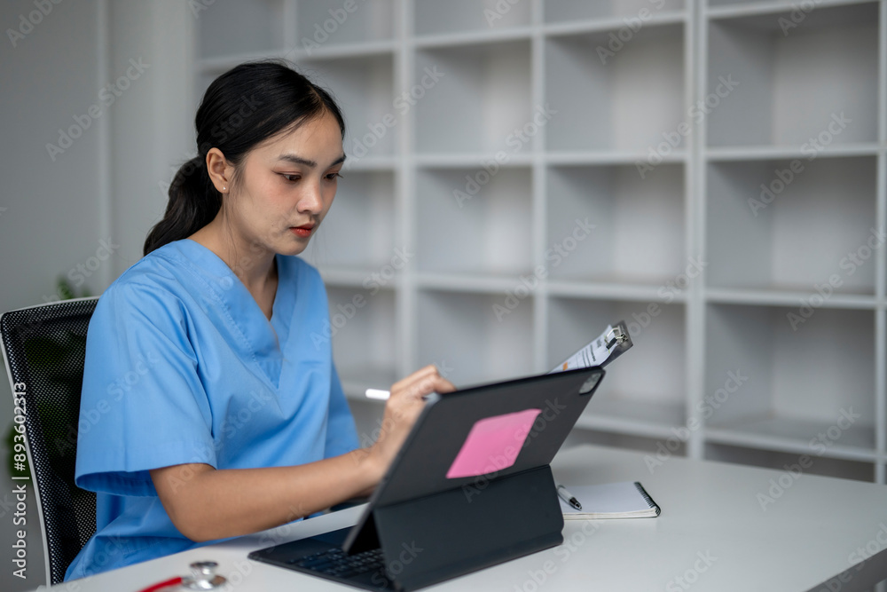 A woman in a blue scrubs is sitting at a desk with a laptop A woman in a blue scrubs is sitting at a desk with a laptop