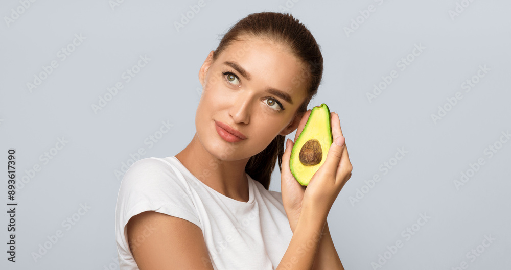 Beautiful Lady Holding Half Of Avocado Near Face Standing On White Studio Background. Beauty And Healthy Oils Concept. Panorama Beautiful Lady Holding Half Of Avocado Near Face Standing On White Studio Background. Beauty And Healthy Oils Concept. Panorama