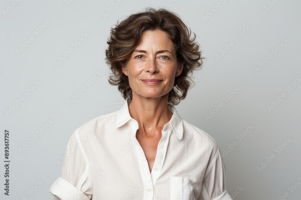 Portrait of a content woman in her 50s wearing a simple cotton shirt over white background Portrait of a content woman in her 50s wearing a simple cotton shirt over white background