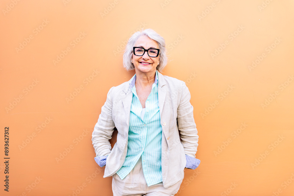 stylish mature woman smiling happy looking at camera leaning on an orange wall, concept of active lifestyle in adulthood, copyspace for text stylish mature woman smiling happy looking at camera leaning on an orange wall, concept of active lifestyle in adulthood, copyspace for text