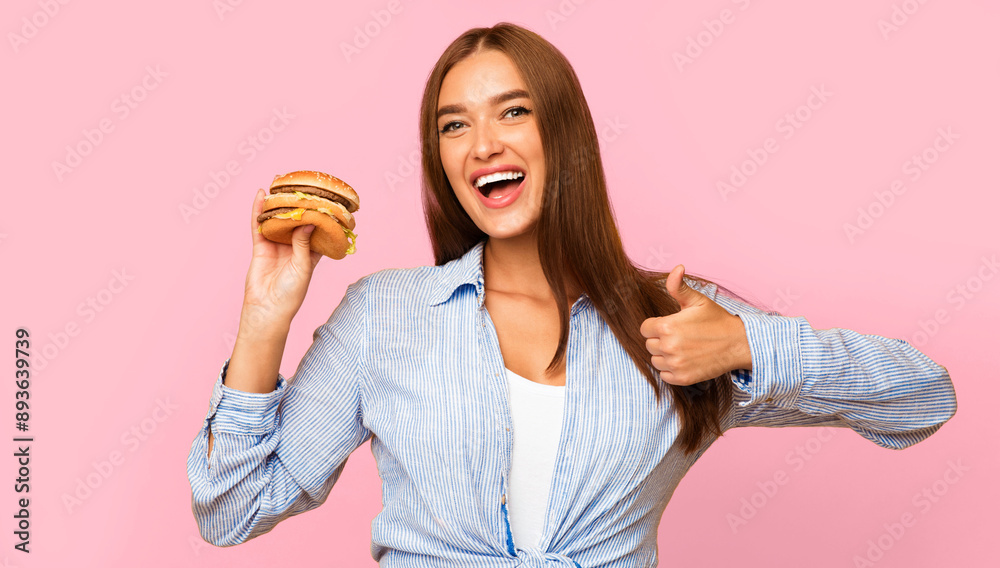 I Like Fast Food. Smiling Girl Holding Burger Gesturing Thumbs Up Standing On Yellow Studio Background I Like Fast Food. Smiling Girl Holding Burger Gesturing Thumbs Up Standing On Yellow Studio Background