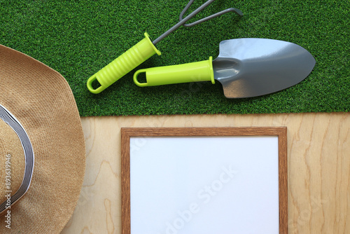 Gardening, composition of objects, flat lay. Gardening tool, frame for photo or text and summer hat on a background of grass and wood texture. World Environment Day. Top view. Spring gardening concept