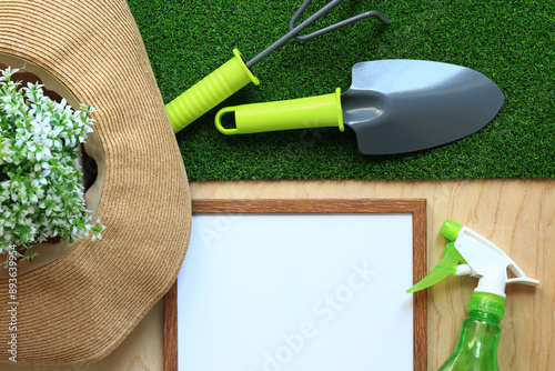Gardening, composition of objects, flat lay. Gardening tool, frame for photo or text and summer hat on a background of grass and wood texture. World Environment Day. Top view. Spring gardening concept