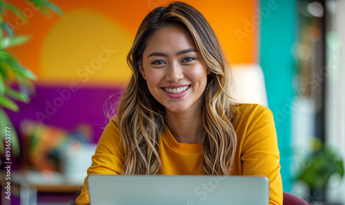 young Filipino woman working on laptop in a modern colorful office/ work from home, remote worker / digital nomad
