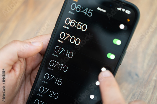 Obraz na płótnie Person toggling alarms on a smartphone screen with a blurred wooden background