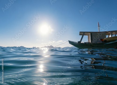 A small boat is moored in calm blue waters on a sunny day, with distant islands visible on the horizon.