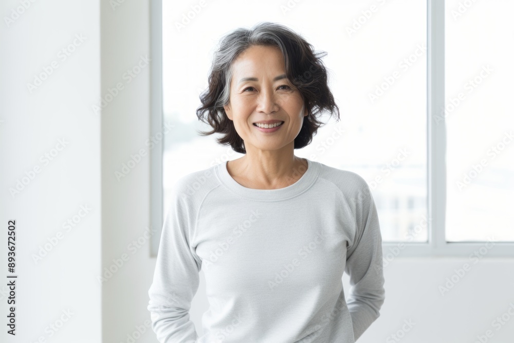 Portrait of a satisfied asian woman in her 60s showing off a lightweight base layer in modern minimalist interior Portrait of a satisfied asian woman in her 60s showing off a lightweight base layer in modern minimalist interior