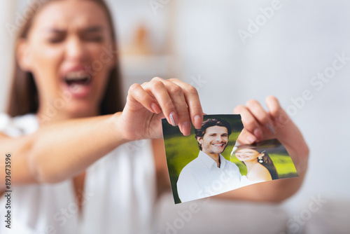 Breakup. Angry Girl Tearing Apart Photo Of Happy Moments With Ex-Boyfriend After Quarrel And Seperation Sitting Indoor. Selective Focus