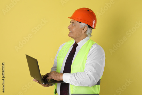 Engineer in hard hat with laptop on yellow background © New Africa