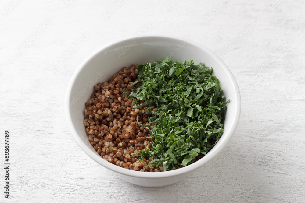 White bowl with boiled buckwheat and kale on a gray background, top view. Healthy homemade vegan food White bowl with boiled buckwheat and kale on a gray background, top view. Healthy homemade vegan food