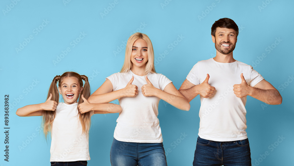 A family of three, a young girl, a woman, and a man, stand in a row in front of a blue background. They all smile brightly and hold their thumbs up in the air. A family of three, a young girl, a woman, and a man, stand in a row in front of a blue background. They all smile brightly and hold their thumbs up in the air.