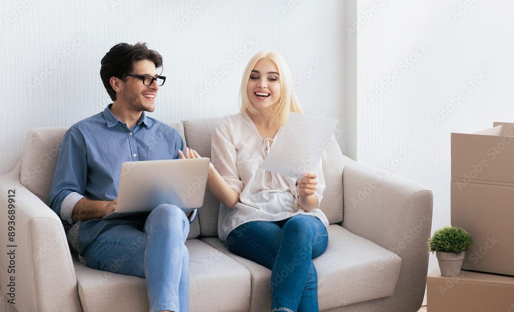 A young couple sits on a couch, discussing home improvement plans. The woman holds paperwork while the man uses a laptop. A young couple sits on a couch, discussing home improvement plans. The woman holds paperwork while the man uses a laptop.