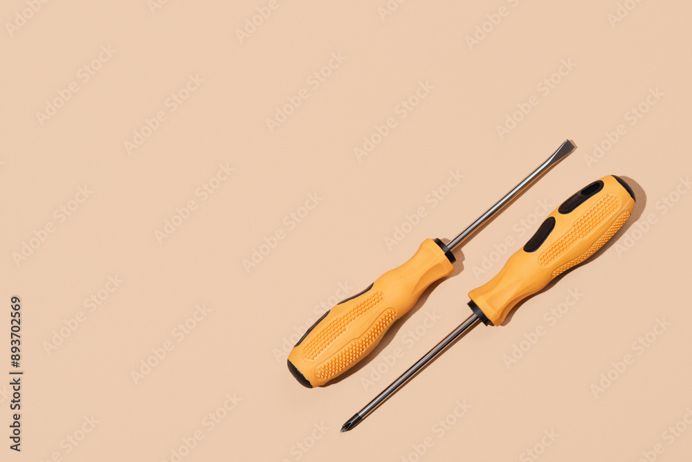 Two screwdrivers with yellow and black handle on beige background. Labor Day concept Two screwdrivers with yellow and black handle on beige background. Labor Day concept