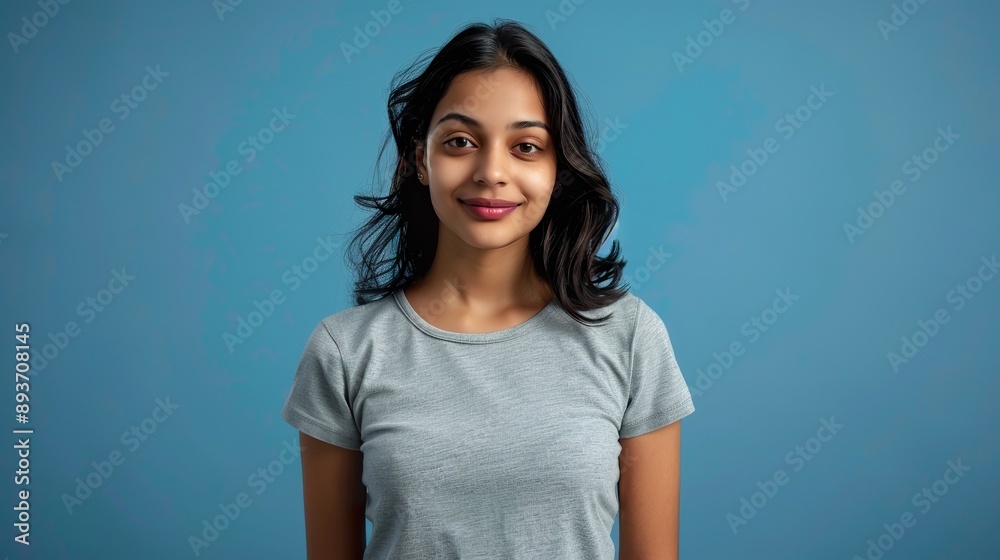 a good-looking young Indian student girl with dark hair, wearing a grey t-shirt and jeans, against a blue background 