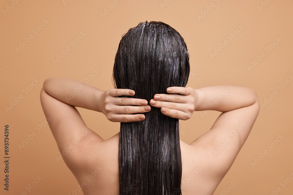 Woman applying hair mask on beige background, back view Woman applying hair mask on beige background, back view