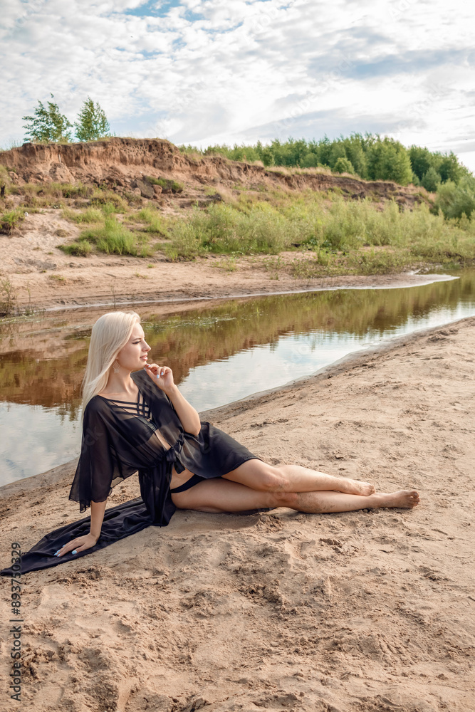 A girl sits on a sandy beach in a black swimsuit and cape. A girl sits on a sandy beach in a black swimsuit and cape.