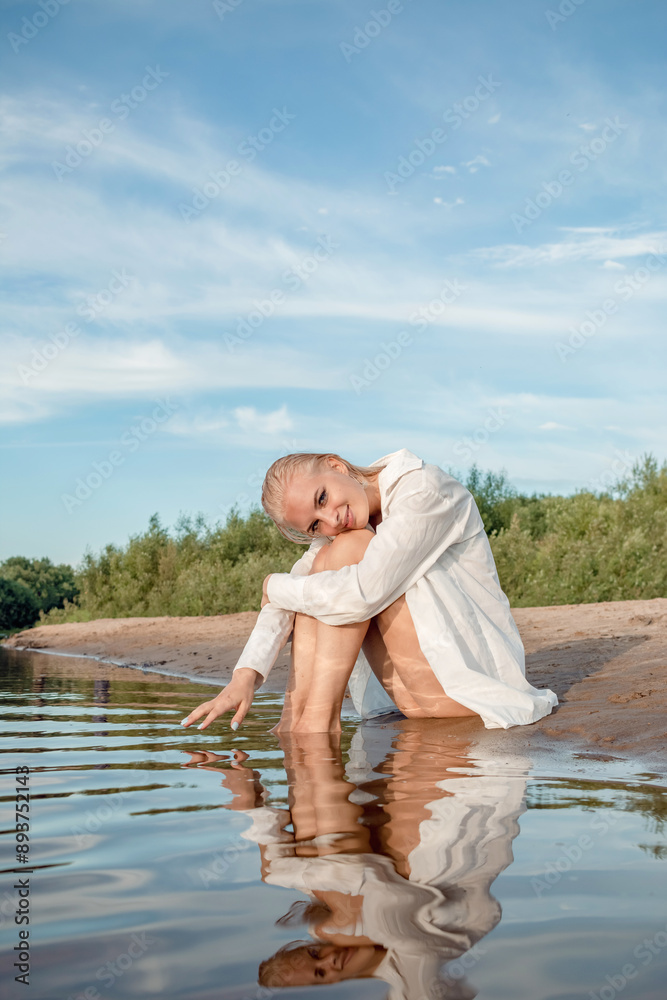 Naklejka premium A girl in a white shirt sits on the shore.