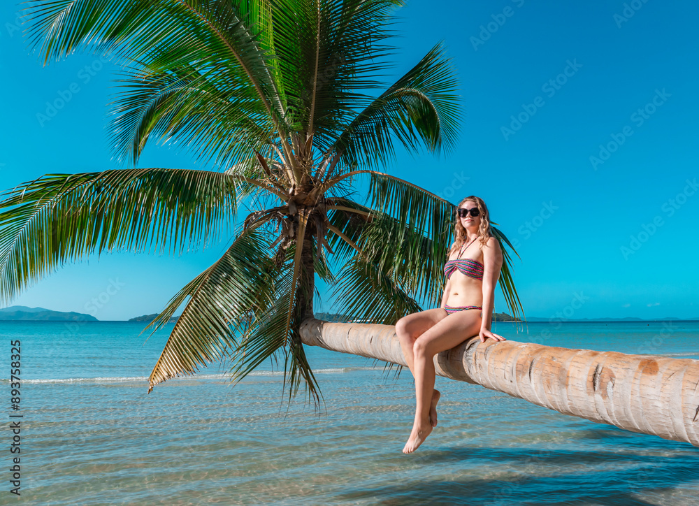 Woman sitting on a palm tree trunk over tropical waters Woman sitting on a palm tree trunk over tropical waters