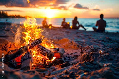 A roaring bonfire crackles on a sandy beach at sunset. Blurred silhouettes of people gather around the flames, enjoying the warmth and the view