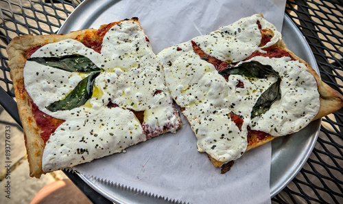 two square slices of sicilian style pizza (fresh white mozzarella basil leaves thin crust) on round tray with parchment paper (italian food) red pepper flakes red sauce photo