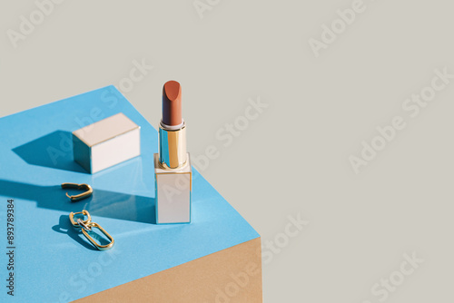 Minimal style composition made of lipstick and golden earrings. Makeup and beauty concept background.