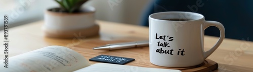 Close-up of a coffee mug with 'Let's talk about it' text next to a notebook and a pen, creating a cozy workspace vibe.