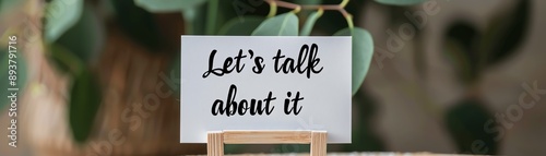 Close-up of a white sign with 'Let's talk about it' written on it, placed on a small easel. Ideal for communication and discussion themes.