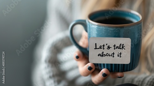 Close-up of a woman holding a coffee mug with a 'Let's talk about it' note, symbolizing communication and support through conversation.