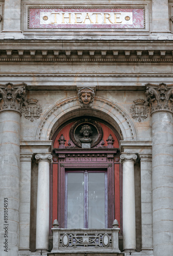 Admiring the exquisite facade of the Lyon Theater, with its tall red-framed windows, intricate stone sculptures, and elegant marble plaque.