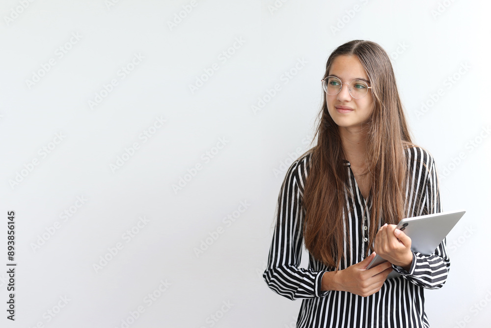 Pensive teenage girl, student, young business lady holding digital tablet and standing on light background, copy space. Place for text. Pensive teenage girl, student, young business lady holding digital tablet and standing on light background, copy space. Place for text.