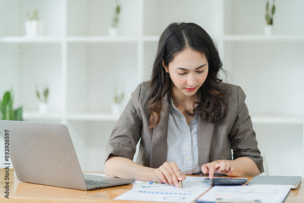 Focused Businesswoman: A professional woman in a suit analyzes financial data on a calculator, showcasing her dedication and focus in the workplace. Focused Businesswoman: A professional woman in a suit analyzes financial data on a calculator, showcasing her dedication and focus in the workplace.