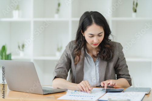 Focused Businesswoman: A professional woman in a suit analyzes financial data on a calculator, showcasing her dedication and focus in the workplace. 