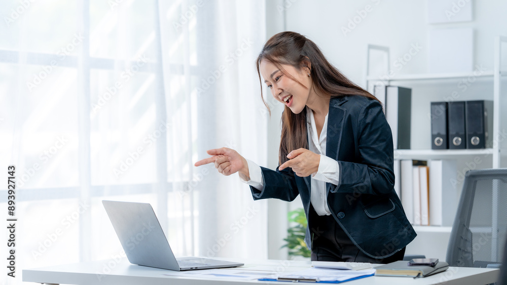 Excited Asian young woman using phone and laptop sitting on a desk office in the day at office Excited Asian young woman using phone and laptop sitting on a desk office in the day at office