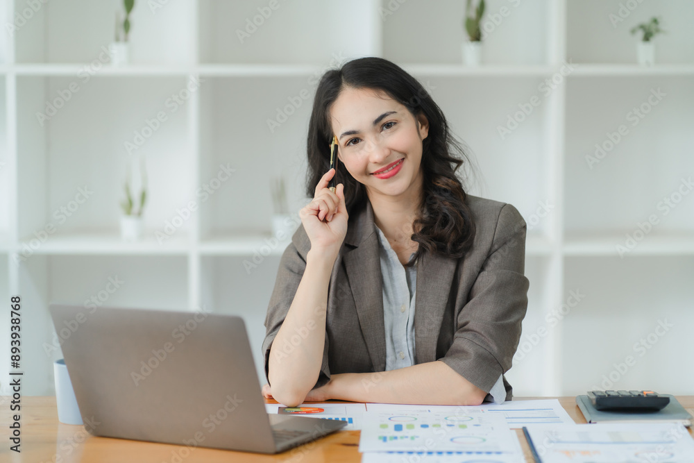 Beautiful business woman smiling while working on laptop and holding documents in hand Beautiful business woman smiling while working on laptop and holding documents in hand