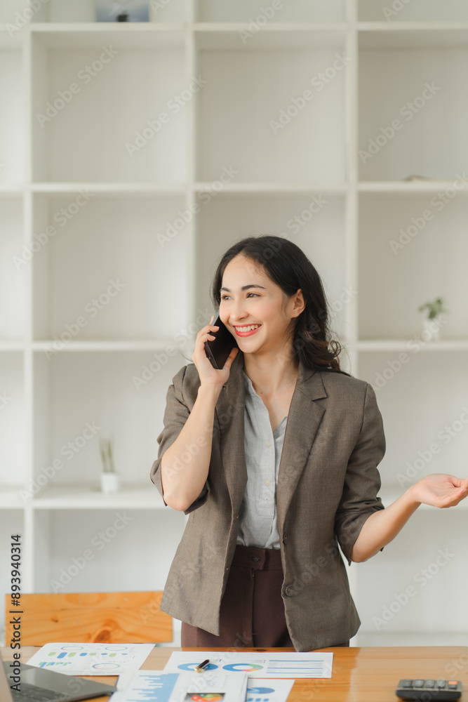 Young charming Asian businesswoman having a phone call with her client while working in the office room. Young charming Asian businesswoman having a phone call with her client while working in the office room.