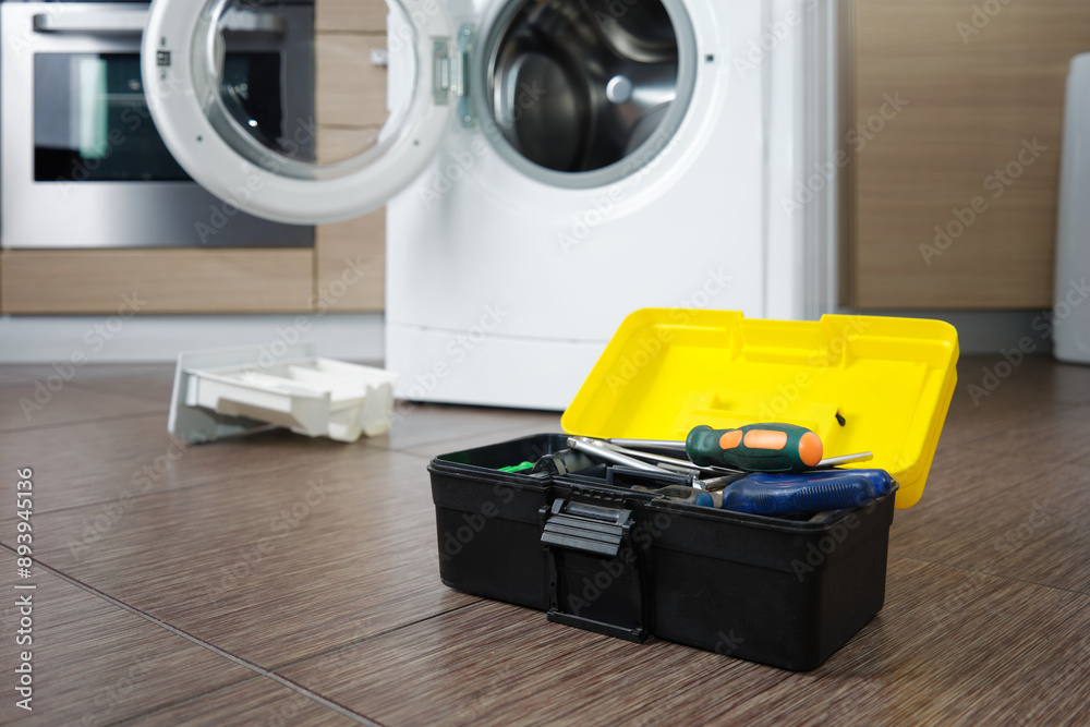 Close-up of a set of professional tools against the background of a disassembled washing machine in the kitchen. Close-up of a set of professional tools against the background of a disassembled washing machine in the kitchen.