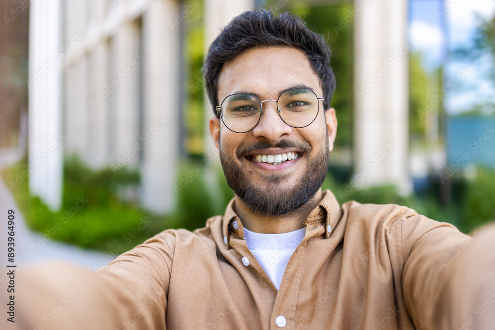 © Liubomir - Close-up of smiling man taking selfie outdoors on sunny day. Man with beard and glasses in casual clothing enjoying outdoor moment. Concept of happiness, modern communication, and casual lifestyle.