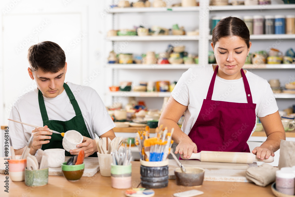 Fototapeta premium Young man and young woman making pottery from clay in workshop