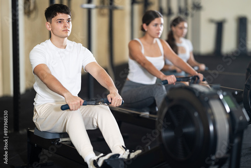 Young guy in sportswear training his arms using machine in gym © JackF