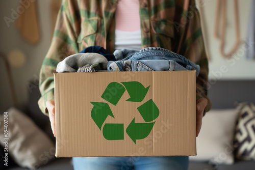 Person holding cardboard box with recycling symbol, sustainable living, donating clothes for reuse, eco-friendly and environmental conservation concept photo