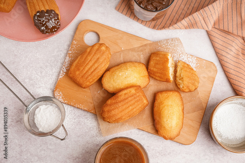 Wooden board with baking paper and delicious madeleines on white background photo