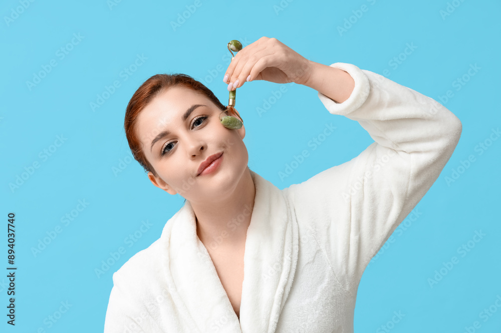 Beautiful young woman using facial massage roller on blue background Beautiful young woman using facial massage roller on blue background