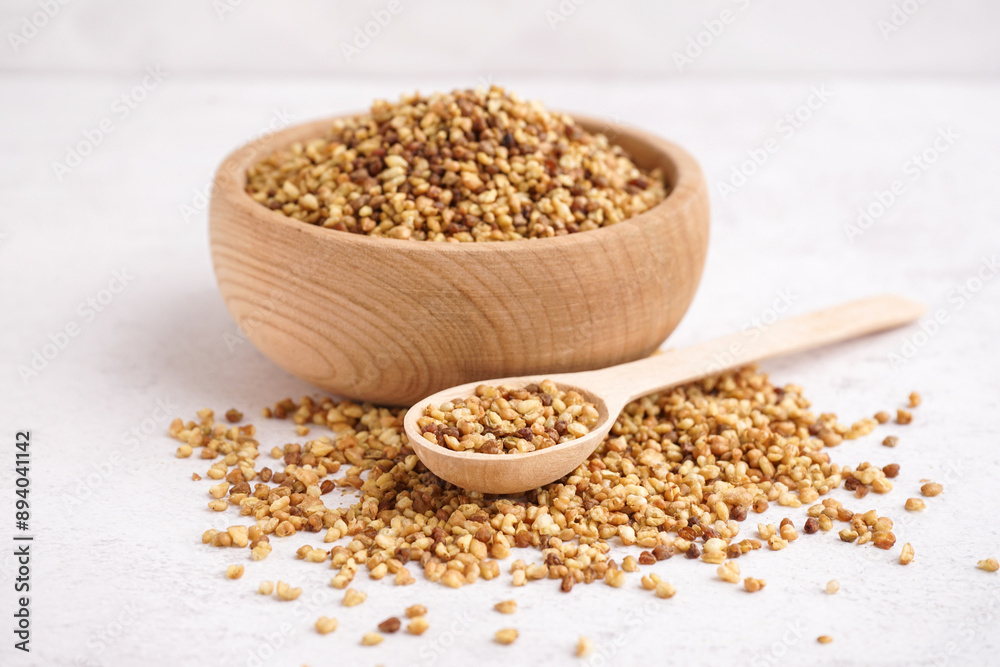Wooden bowl and spoon with raw buckwheat grains on light background Wooden bowl and spoon with raw buckwheat grains on light background