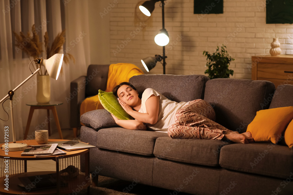 Obraz premium Young woman in pajamas sleeping on cozy sofa in living room at night