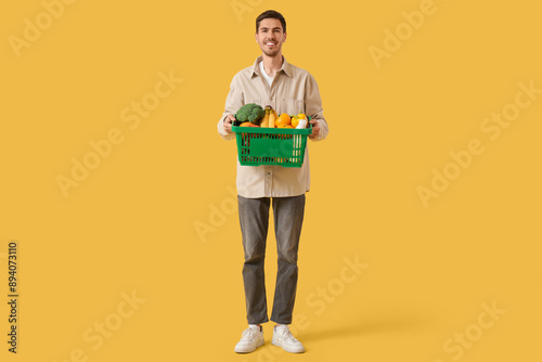 Young man with full shopping basket on yellow background