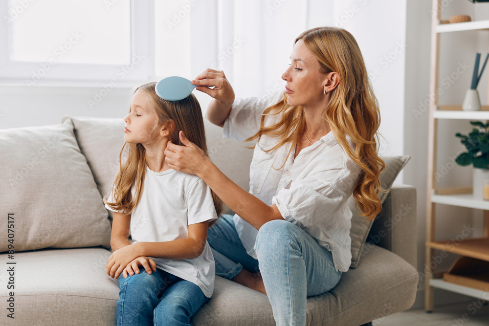 Mother and daughter bonding time as they sit on a cozy couch in the living room, combing hair lovingly Mother and daughter bonding time as they sit on a cozy couch in the living room, combing hair lovingly