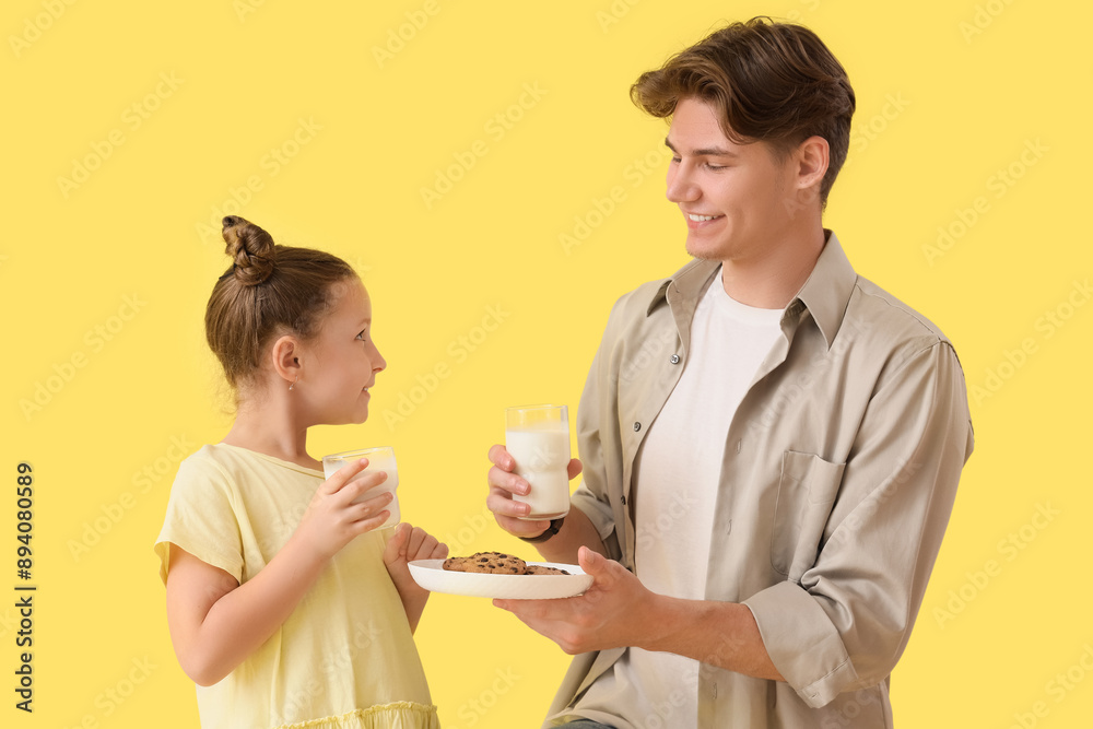 Little girl and her father holding glasses of milk with cookies on yellow background Little girl and her father holding glasses of milk with cookies on yellow background