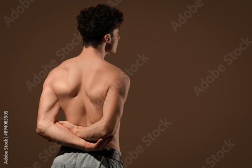 Muscular young man on dark brown background, back view