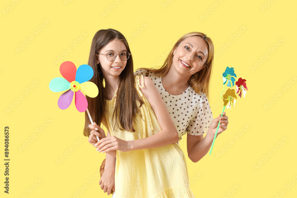 Teenage girl and her mother with toy windmills on yellow background Teenage girl and her mother with toy windmills on yellow background